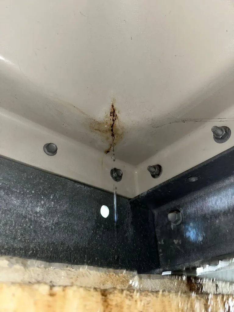 Water leaking through a crack near the bottom corner of a sectional water tank panel
